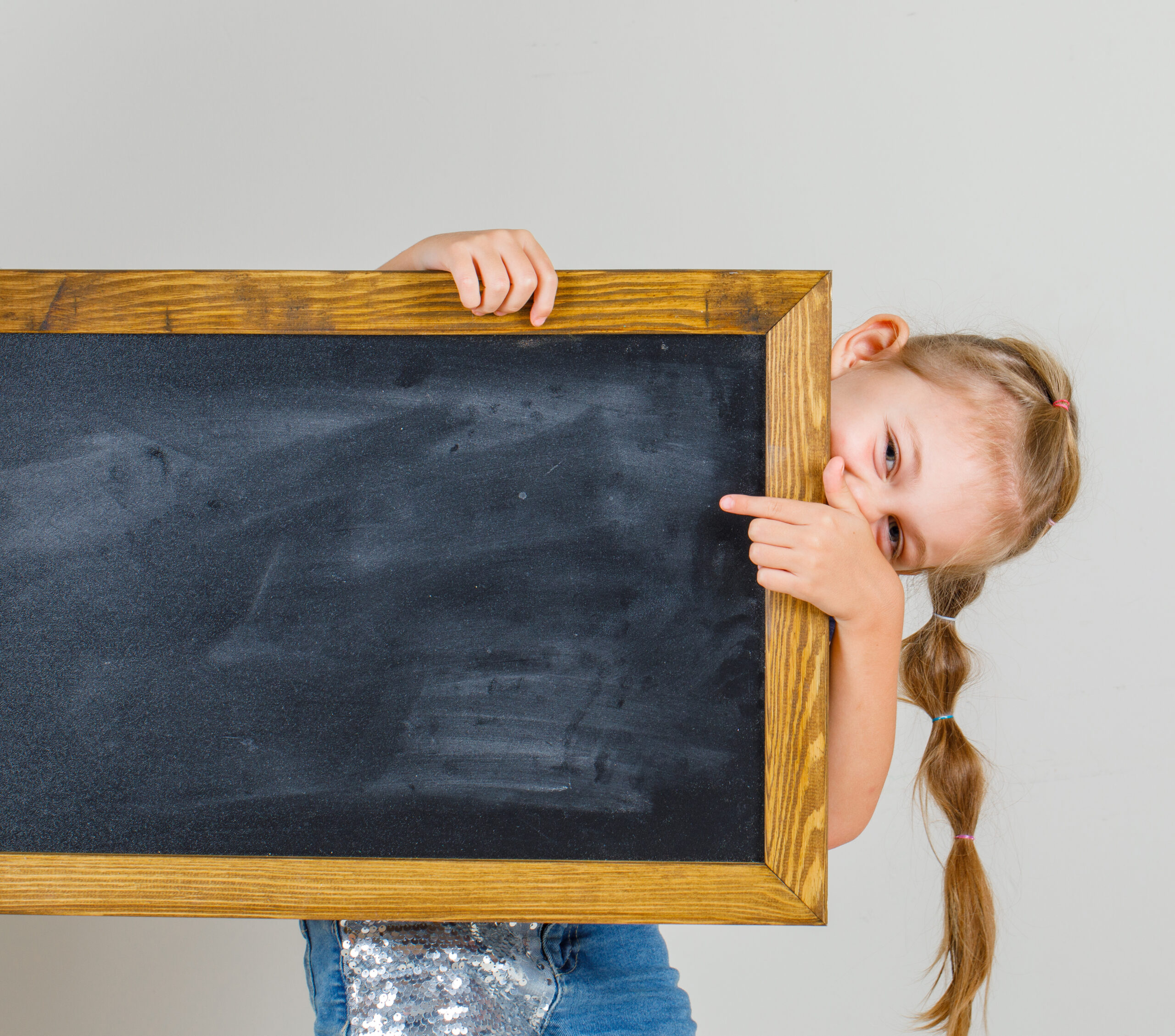 Little girl pointing at blackboard in t-shirt and denim skirt and looking happy , front view.